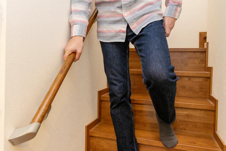 階段の手すりにつかまって膝をかばう女性